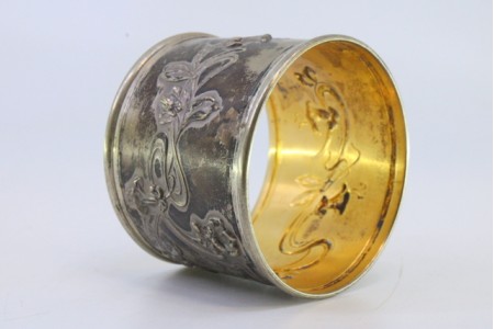 Argola de guardanapo em prata com motivos florais relevados envolvendo cartela para monograma e interior dourado.